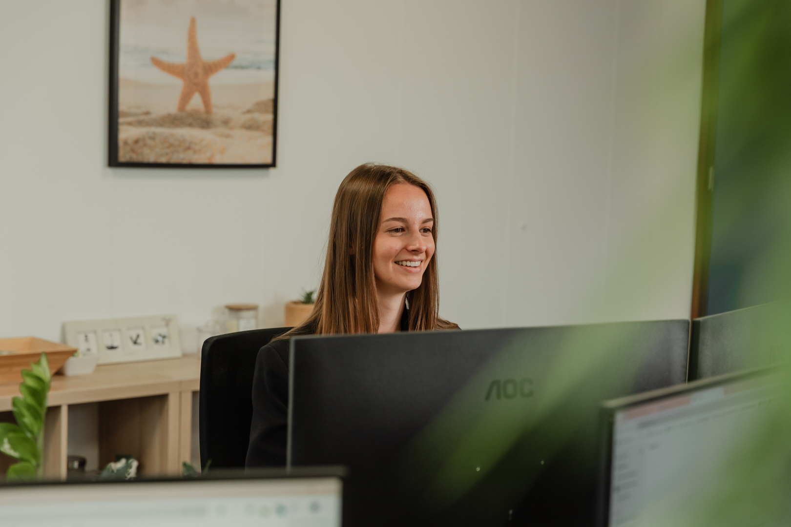 Web Wings medewerkster werkt glimlachend achter haar computer op kantoor.